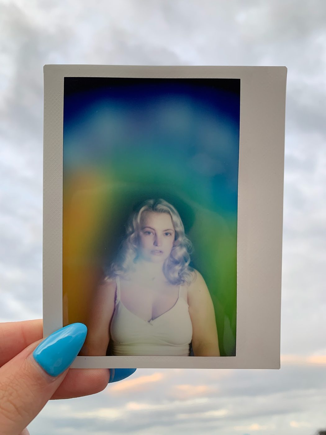 An aura portrait held up against a cloudy sky, glowing blue, green and gold.