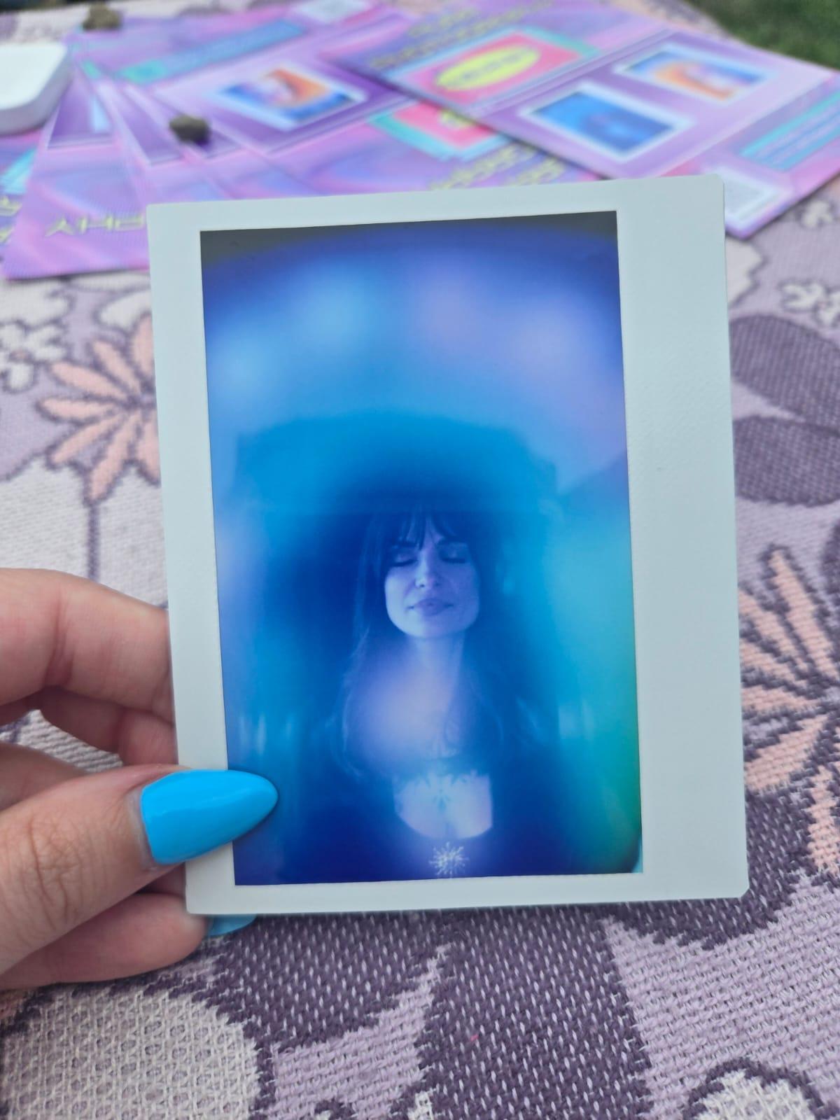 A hand holding an aura portrait of a person with their eyes closed, haloed in deep blue and turquoise.