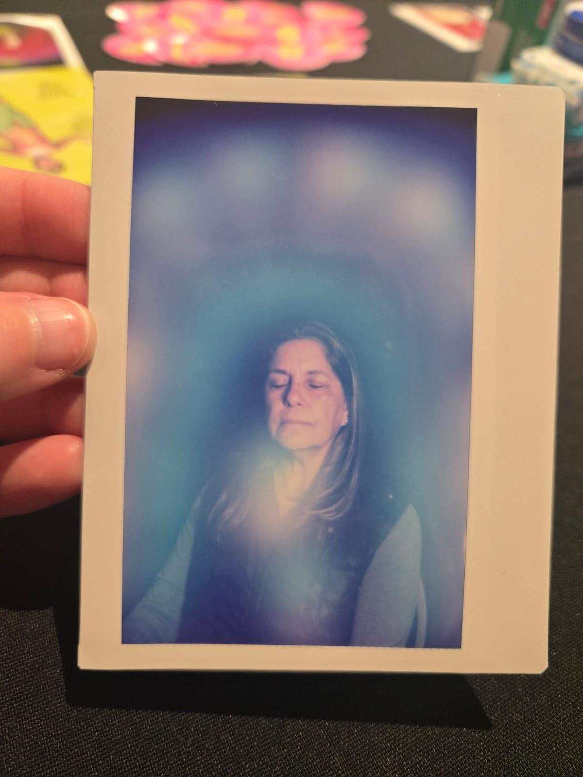 An aura portrait held in one hand, the sitter surrounded by soft blue and violet light.